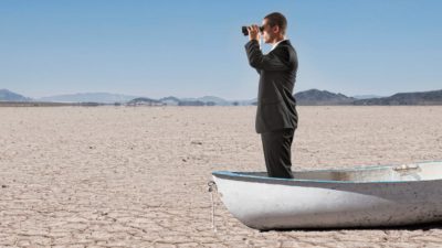 A businessman on a rowing boat marooned on parched land, indicating rocky share price movements on the ASX and better options offshore