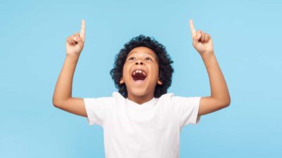 A boy looks up and points his fingers to the sky in celebration pose.