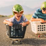Two boys in baskets on skateboards race each along a road.