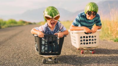 Two boys in baskets on skateboards race each along a road.