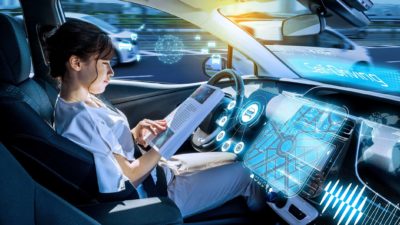 A woman reads a book while her car drives itself, indicating share price movement for ASX share related to electric vehicles