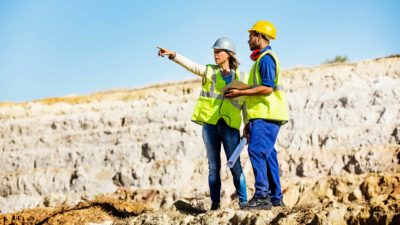 Commodities premium ASX shares Female miner and male miner stand in open mine pit surveying the area