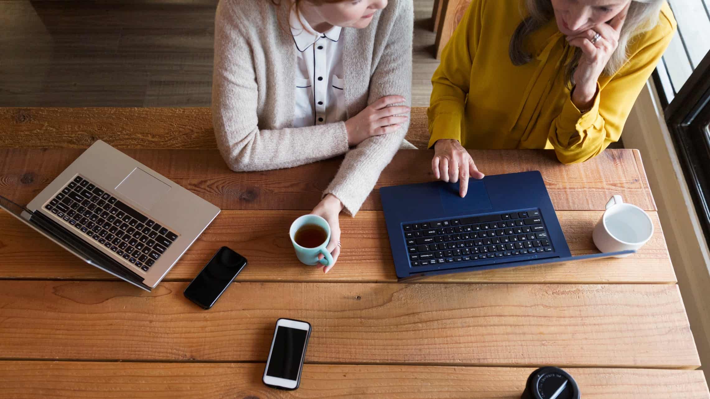 two women having a coffee whilst working from their laptops
