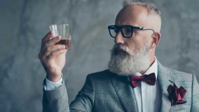A hipster man holds up a glass of whiskey, indicating a share price watch for ASX wine and gin producers
