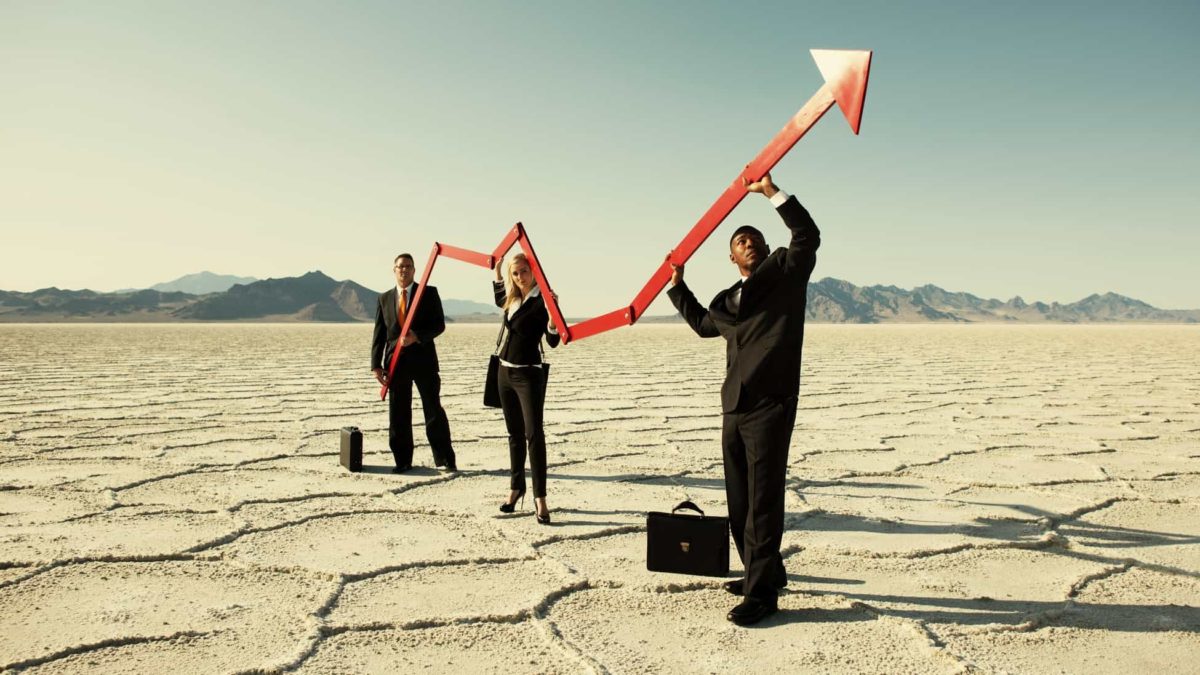 Three businessmen stand in a desert environment holding an upward pointing arrow.