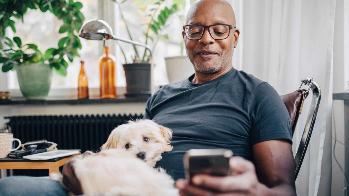 man with dog on his lap looking at his phone in his home.