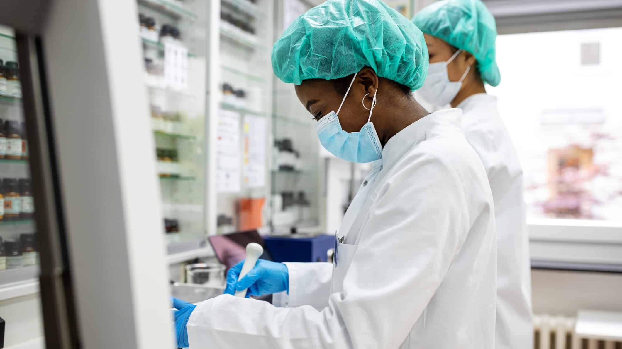 Two staff in a medical research laboratory wearing masks and caps work on their tests, representing the performance of ASX healthcare shares in FY22