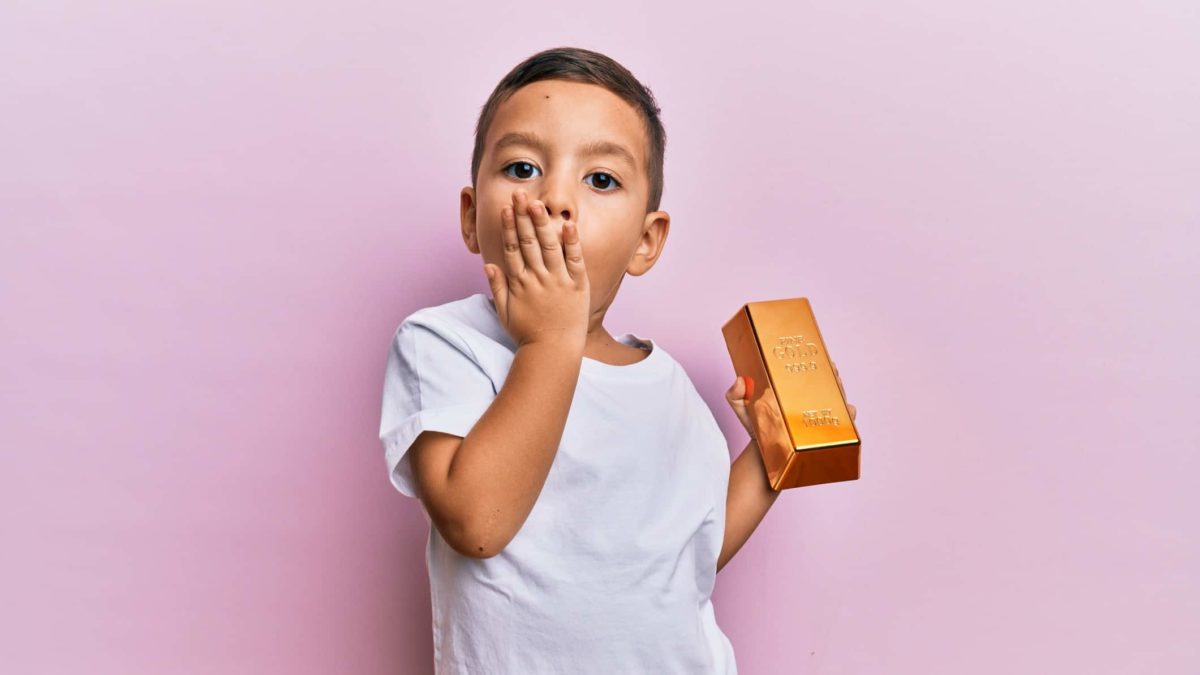 A boy holds a gold bar with a surprised look on his face due to falling ASX gold mining shares including the Newcrest share price