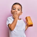 A boy holds a gold bar with a surprised look on his face.