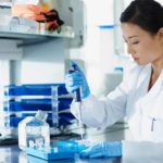 A Sonic Healthcare medical researcher wearing a white coat sits at her desk in a laboratory conducting a COVID-19 test