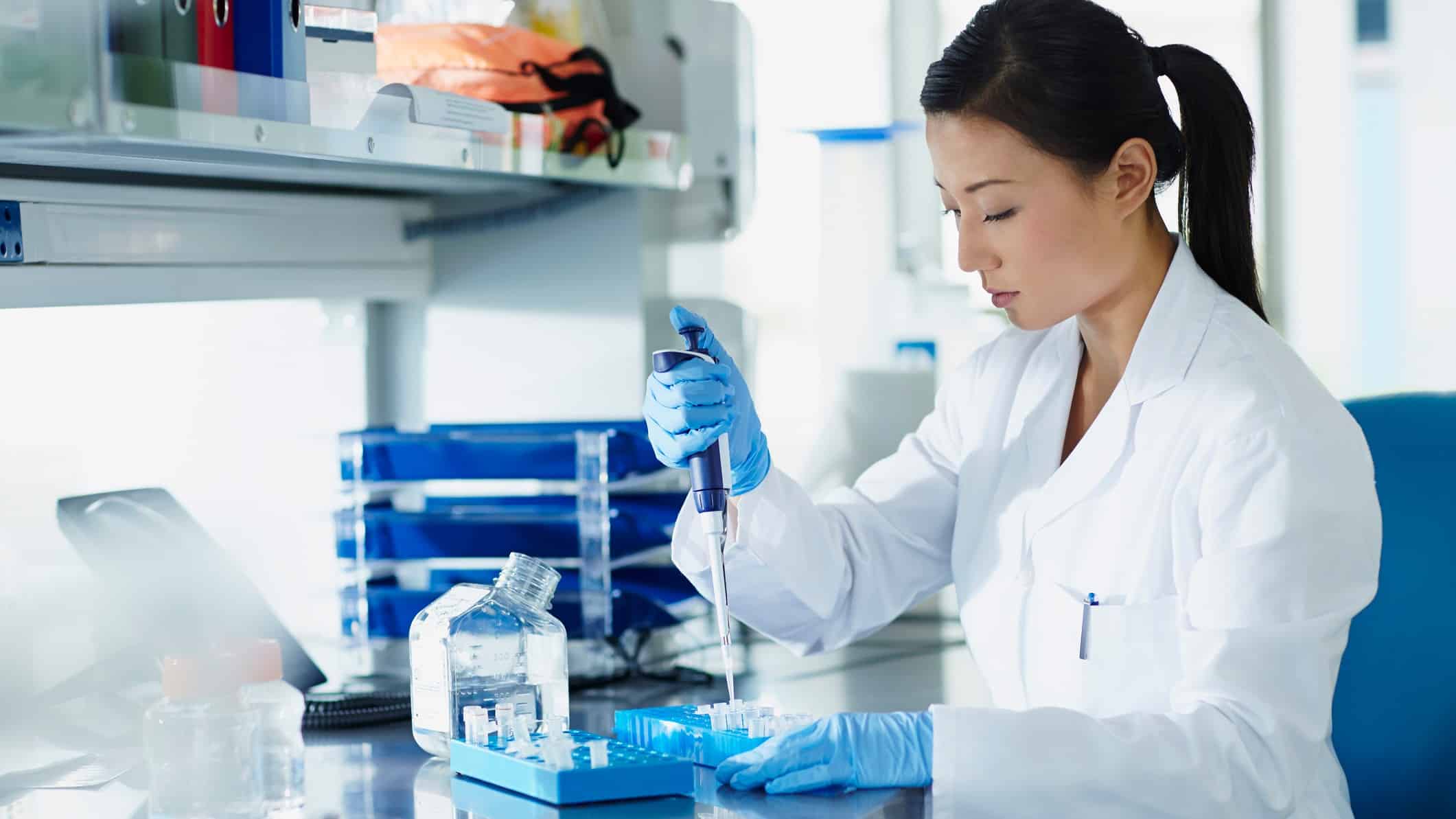 A Sonic Healthcare medical researcher wearing a white coat sits at her desk in a laboratory conducting a COVID-19 test