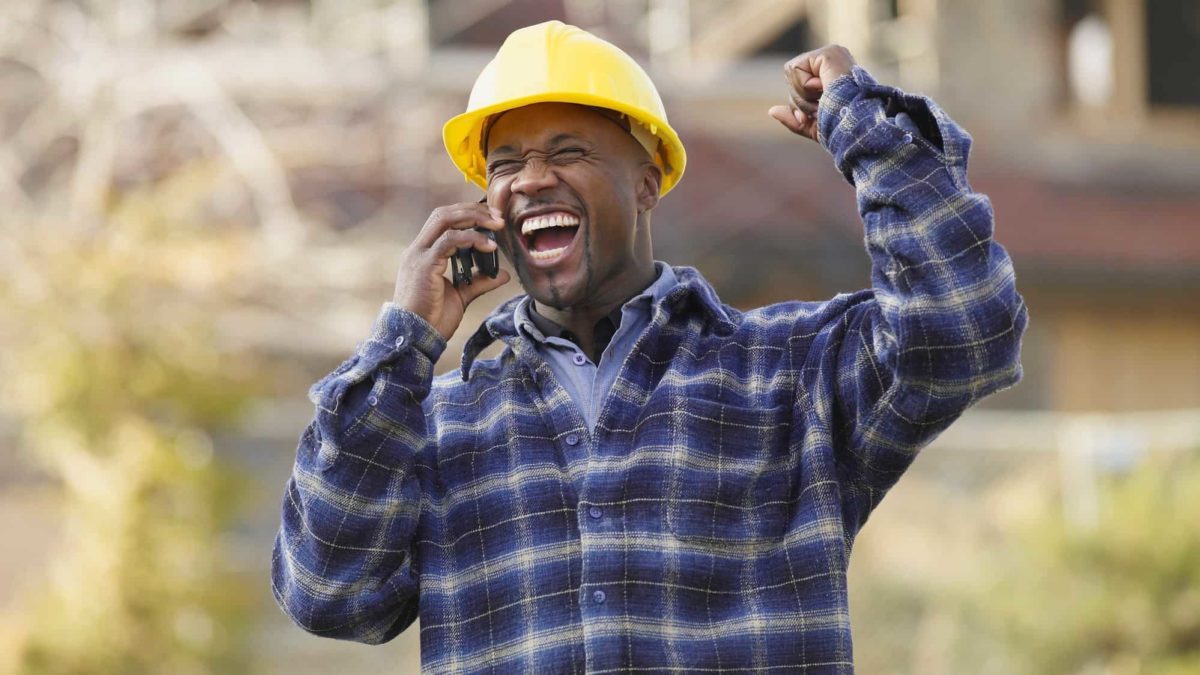 happy engineer/ construction workers raising an arm to celebrate good news from a mobile phone call
