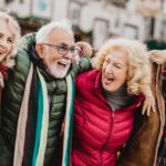 Four senior friends laugh together with arms around each other