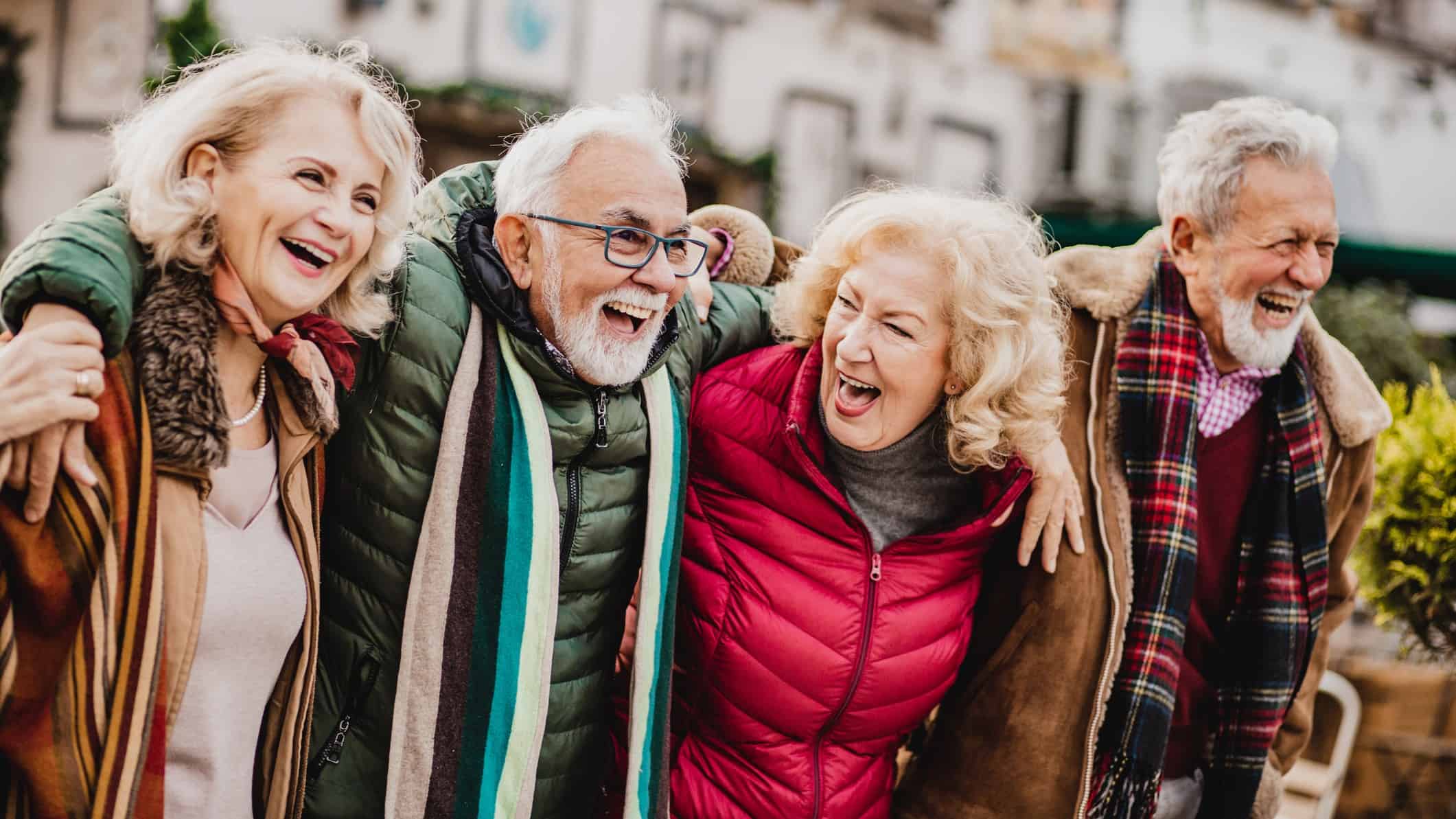 Four senior friends laugh together with arms around each other