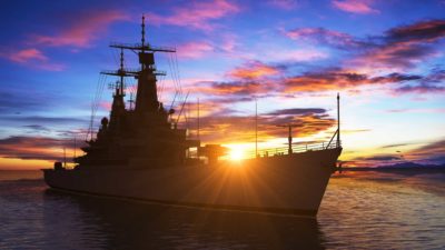 US navy ship sailing along at at sunset