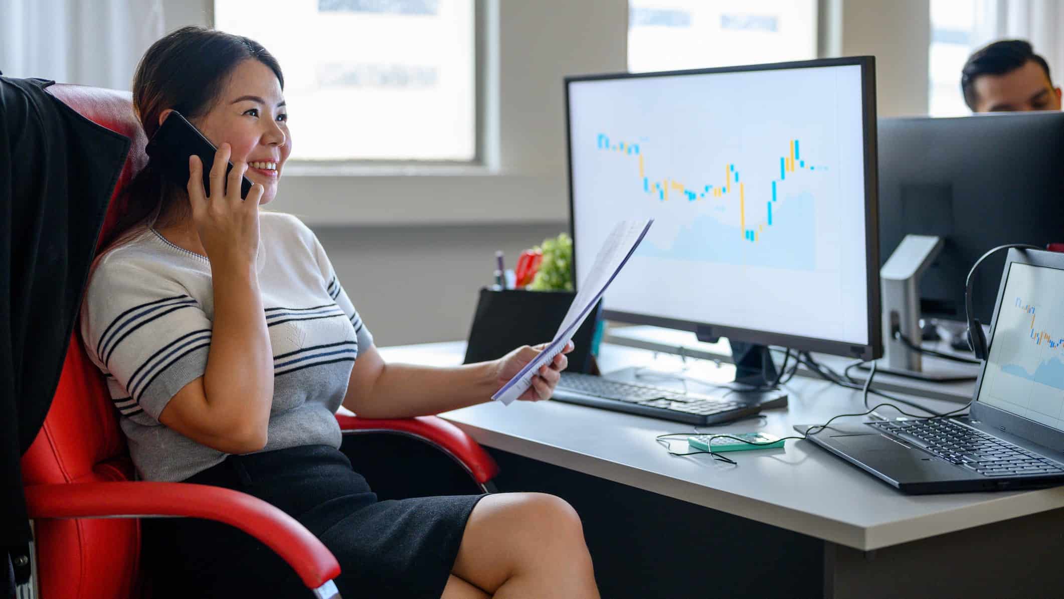 Woman using her mobile phone at her desk with graph on computer