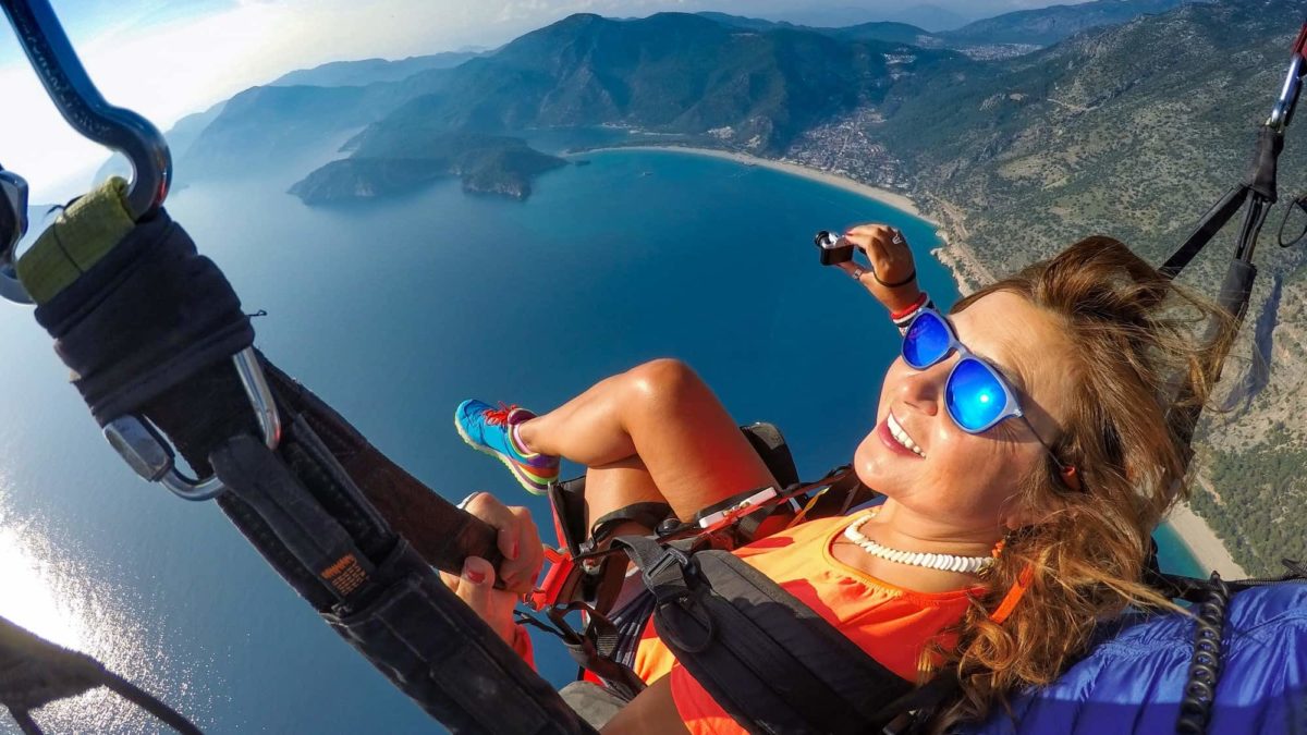 A woman sits back and enjoys the view from a paraglider, indicating share price lifts for ASX travel and adventure shares