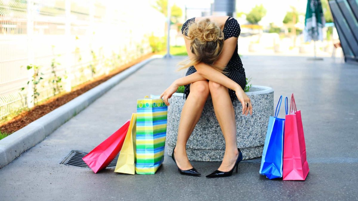 A woman sits with her head down and colourful retail shopping bags all around her.