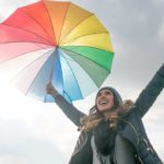 A happy looking woman holding a colourful umbrella against a grey cloudy sky.