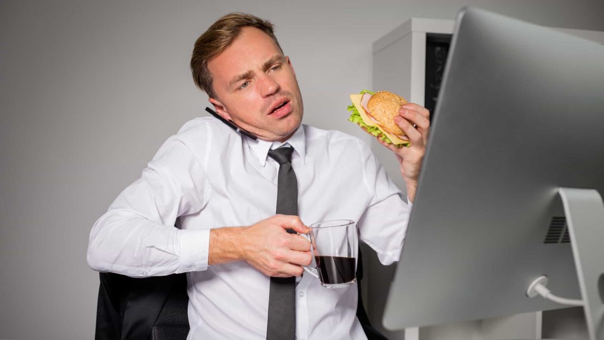 Financial advisor on phone and looking at computer whilst eating and holding coffee