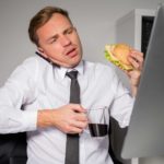 Financial advisor on phone and looking at computer whilst eating and holding coffee