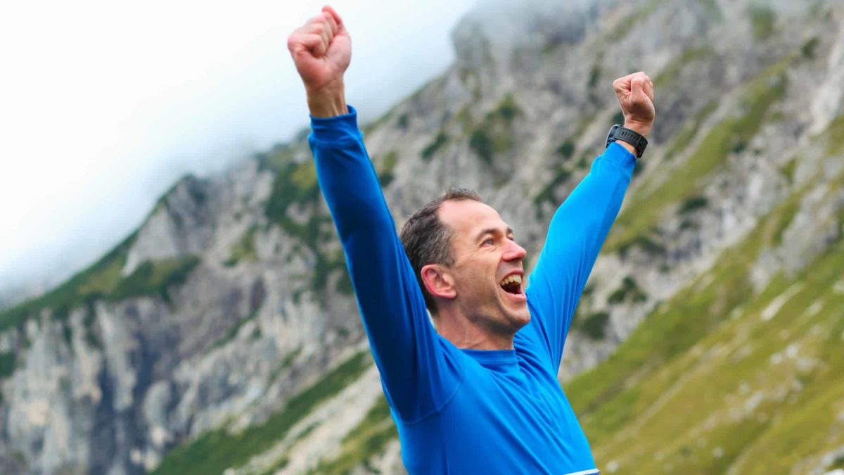 An excited man stretches his arms out above his head as he reaches a mountain peak representing two ASX 200 shares reaching multi-year high prices today