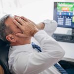 Worried man sitting at desk in front of PC with his head in his hands.