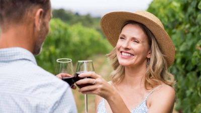 A happy couple drinking red wine in a vineyard as the Treasury Wine share price rises today