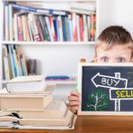 Boy holding chalk board depicting buy and sell options for ASX shares.