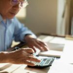 A man sits at his home desk calculating tax on a calculator.
