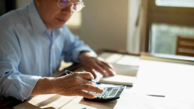 A man sits at his home desk calculating tax on a calculator.