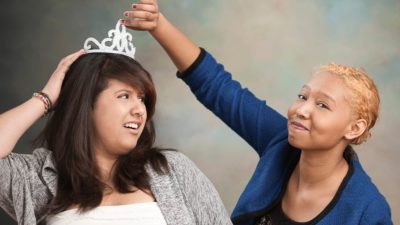 A young woman holds onto her crown as another moves to take it, indicating rival ASX shares