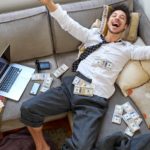 man laying on his couch with bundles of money and extremely ecstatic about high dividend returns