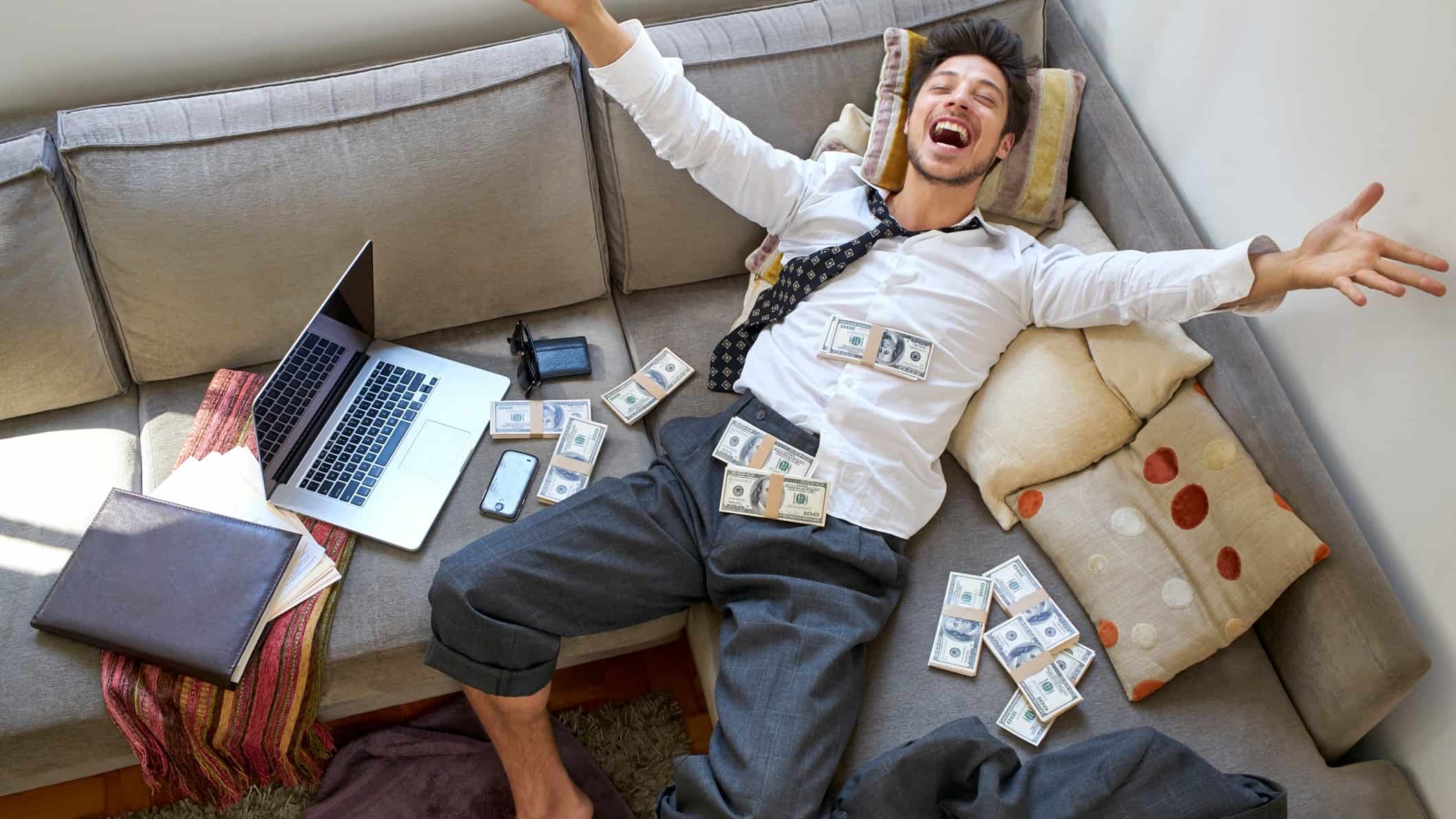 man laying on his couch with bundles of money and extremely ecstatic about high dividend returns