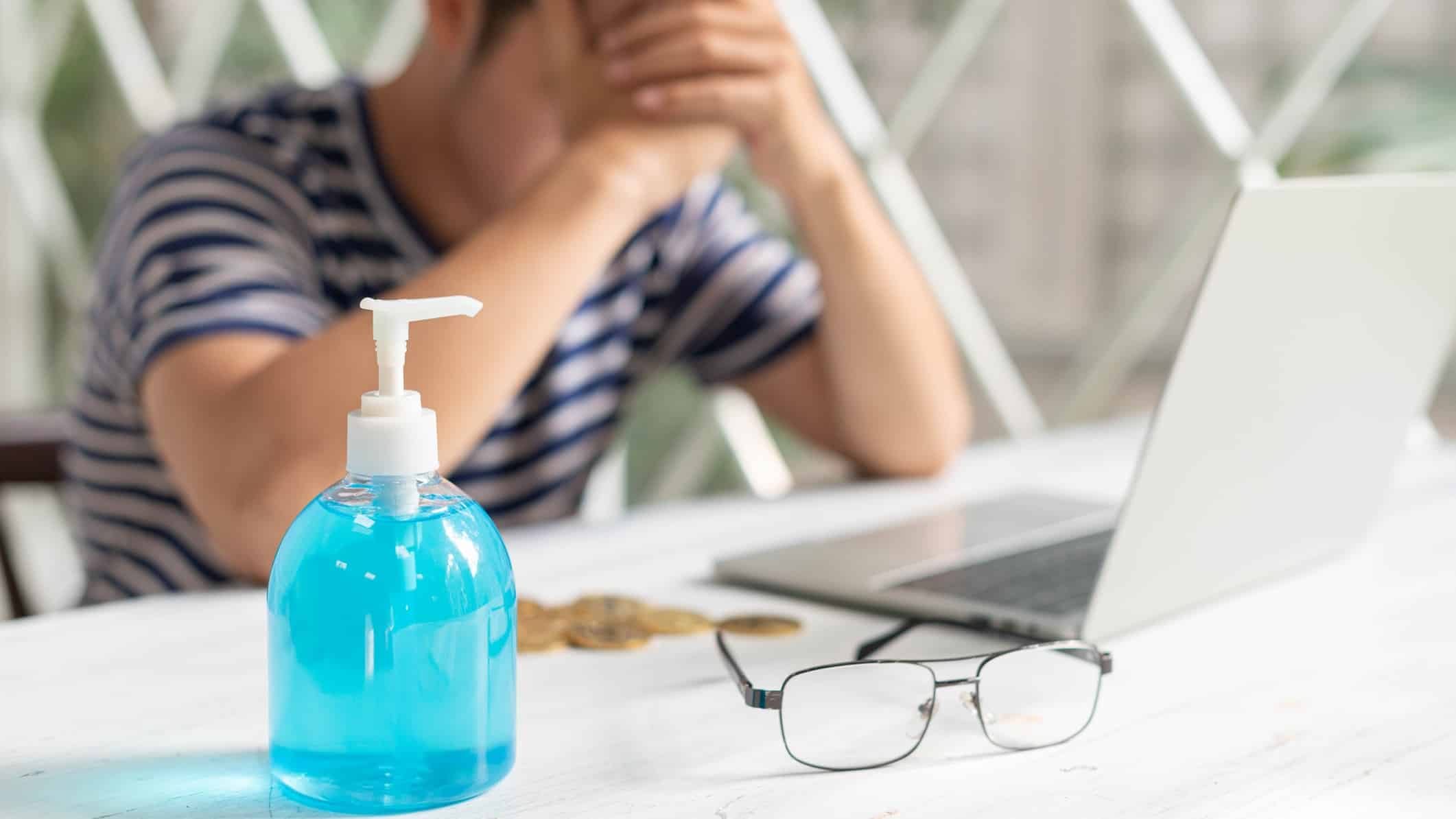 A man at a computers rests his head in his hands with a sanitiser bottle in the foreground