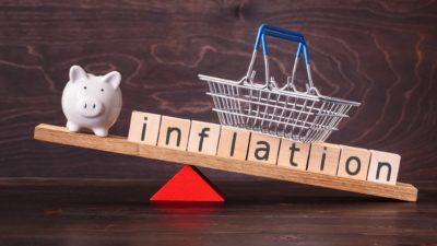inflation written on wooden cubes being balanced with a piggy bank and small shopping basket