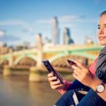 A smiling young woman sits on a bridge in London checking her online shopping, indicating share price movement for ASX BNPL shares overseas.