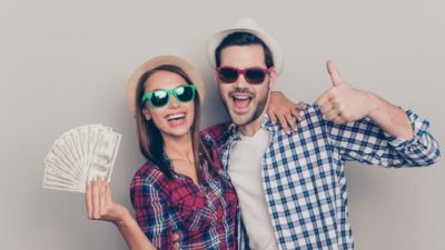 A woman and man hold a wad of money with big smiles on their faces.