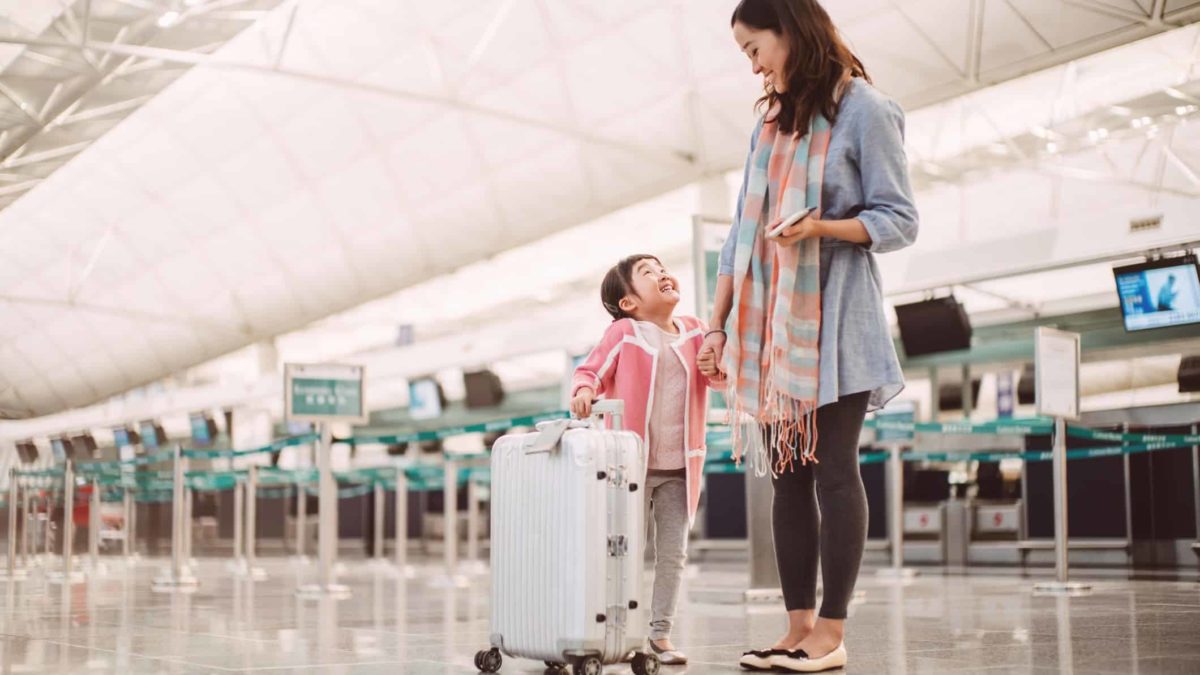 A mum and daughter smiling at each other near an airport check in