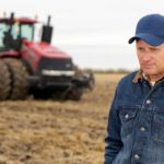 sad and disappointed farmer on a farm with a tractor in the background