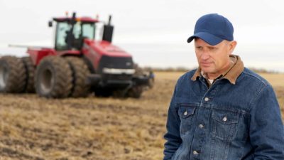 sad and disappointed farmer on a farm with a tractor in the background