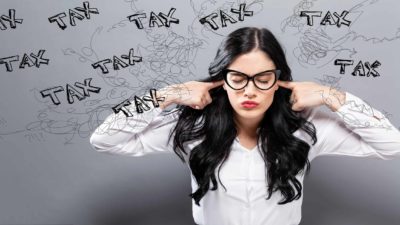 A woman with the word 'tax' scribbled around her, plugs her ears and grimaces, indicating the impact of tax on share price