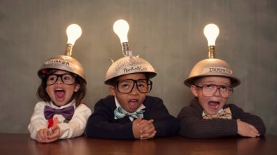 Three children wearing silver thinking hats with light bulbs attached to them.