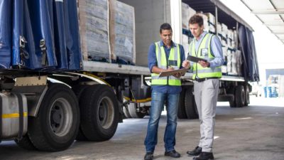 two men talking in front of a transportation truck