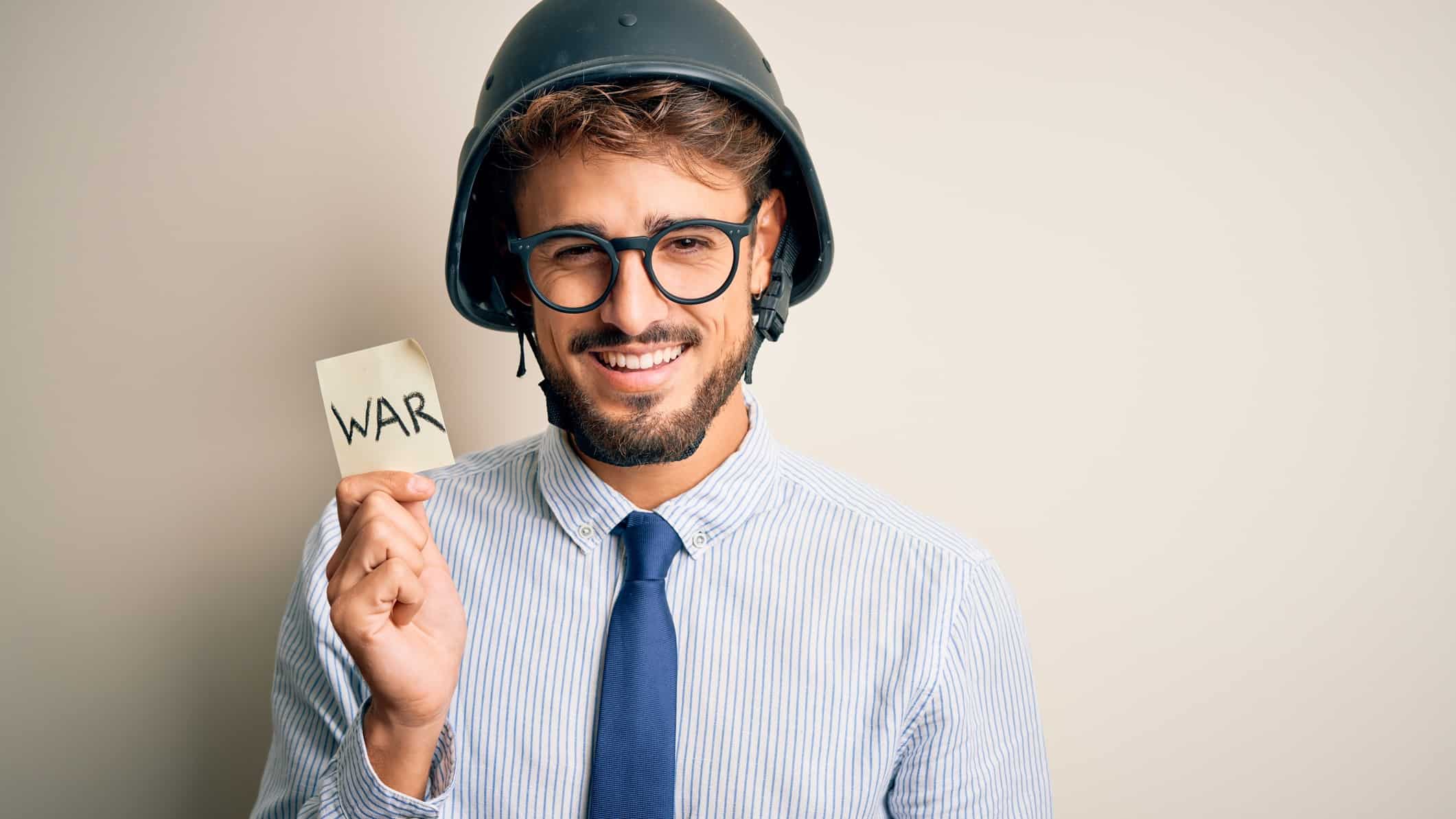 A smiling man wearing a hard hat holds a note that say WAR, indicating share price movement