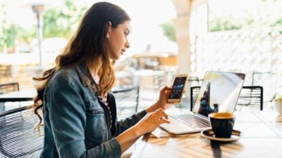 woman looking at iPhone whilst working on a laptop