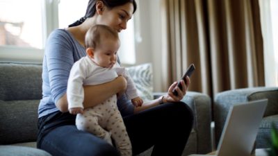 woman holding her baby and looking at her phone happy at the rising share price