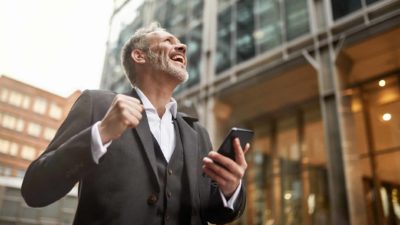 Suncorp share price Businessman cheering and smiling on smartphone