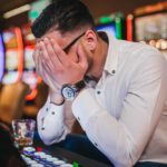 Distressed man at a casino puts his head in his hands, covering his face.