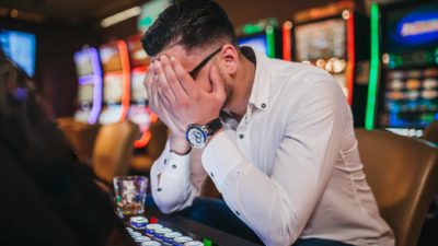 Distressed man at a casino puts his head in his hands, covering his face.